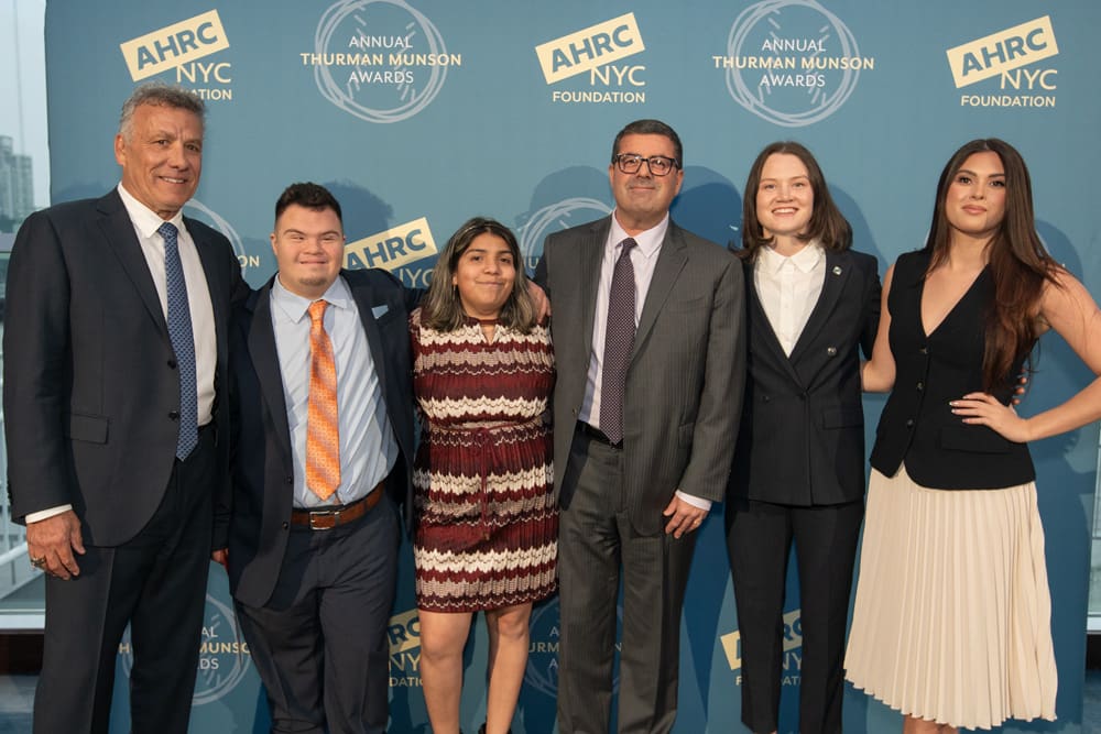 Six people posing for a photo in front of a blue AHRC NYC Foundation step-and-repeat backdrop.